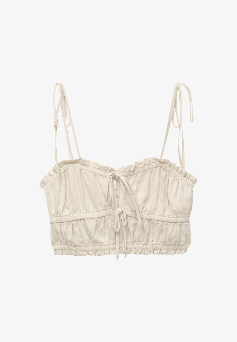 Kort topp i ljus beige tyg, med justerbara axelremmar, rynkade detaljer och snörning framtill.