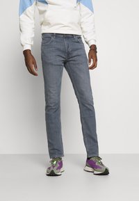 Slim-fit, bleka blå denimjeans med fem fickor och ljus sömnad, bärs med flerfärgade sneakers.
