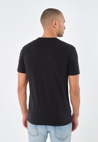 Czarny T-shirt z krótkim rękawem wykonany z bawełny, z okrągłym dekoltem i gładką powierzchnią. Noszony z jasnoniebieskimi dżinsami w luźnym kroju.