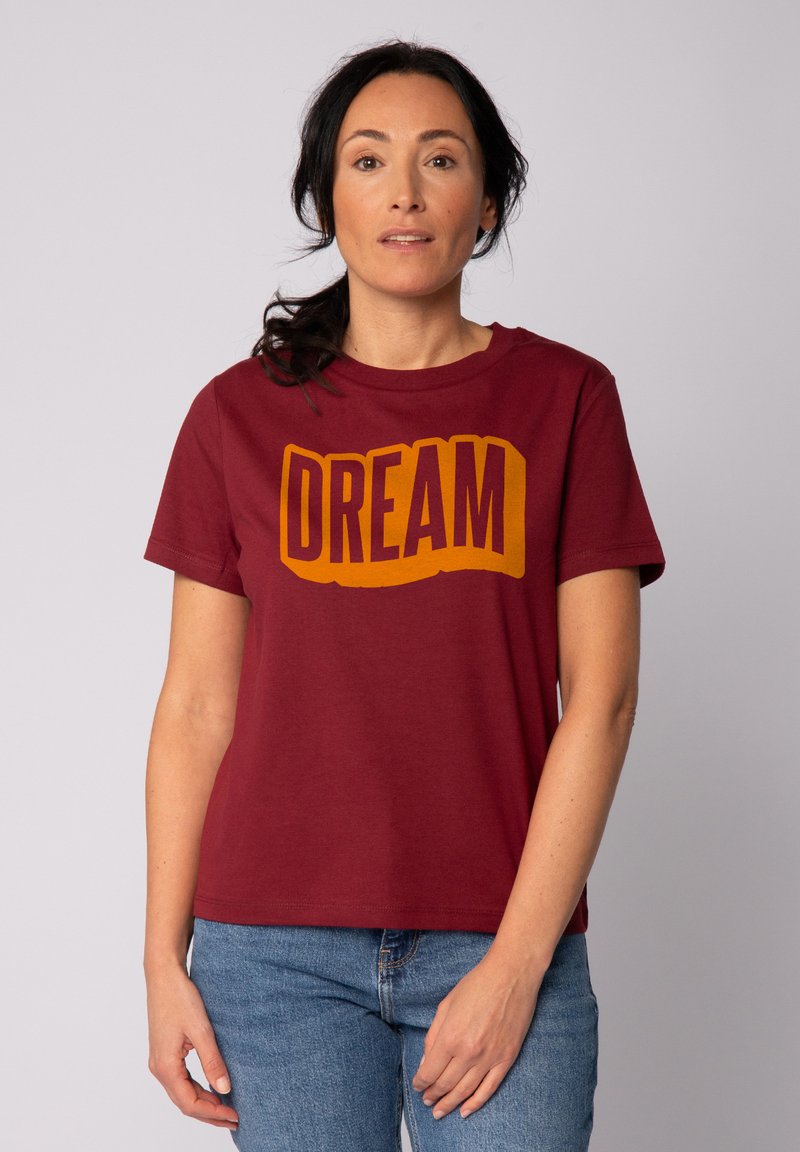 T-shirt en coton bordeaux à manches courtes, avec un grand texte jaune "DREAM" sur la poitrine dans une police en block arrondie.
