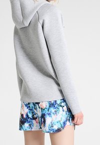 Sweat-shirt à capuche gris à manches longues associé à un short coloré à motifs abstraits bleu, blanc et orange.