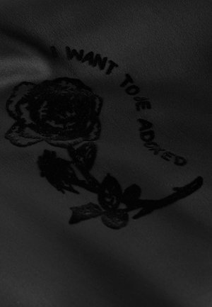 Fekete anyag, amely fekete, texturált rózsamintával rendelkezik, körülötte pedig kör alakban az "HOZZÁAKAROK ADÓDNI" felirat olvasható.