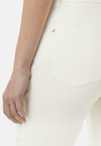 Witte slim-fit jeans met een achterzak voorzien van zilverkleurige hardware. De stof heeft een zachte textuur en minimale zichtbare naden.