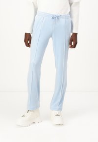 Pantaloni sportivi azzurri chiari con vita elasticizzata, dettagli con cordino, tasche laterali e cuciture laterali a contrasto, abbinati a scarpe da ginnastica bianche e sogliose.