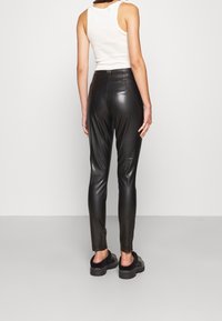 Black faux leather pants with a fitted design, smooth texture, and high waistband. Designed for a slim silhouette and paired with platform shoes.