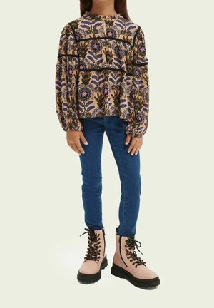 Blusa floral de manga larga en color beige con patrones en púrpura, verde y rosa, combinada con jeans ajustados azules y botas de tobillo en color rosa claro con cordones.