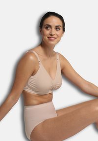 Beige trådlös bh med V-ringning, rynkdetalj i mitten och justerbara axelband. Matchas med höga beige trosor.