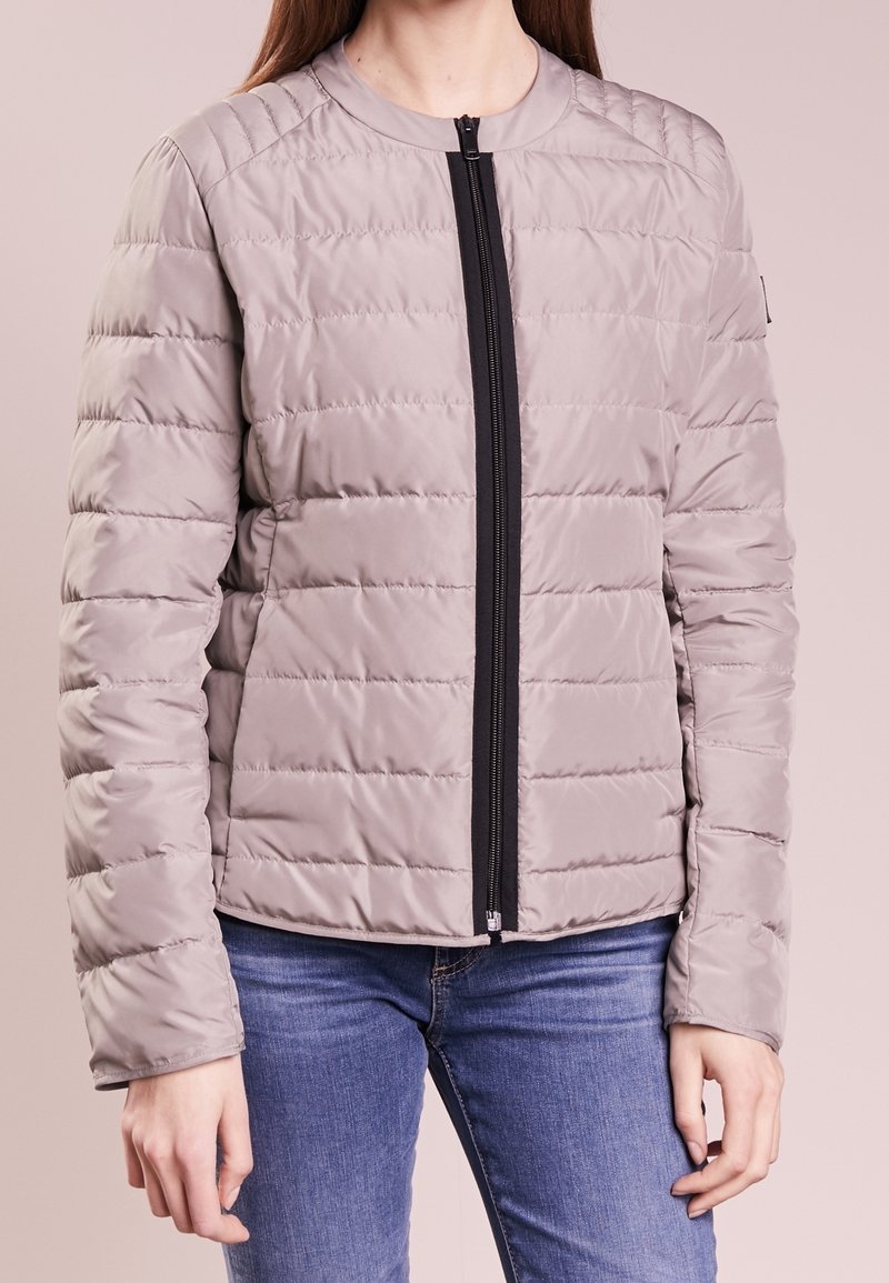 Ljusgrå vadderad jacka med en svart framtill dragkedja, med rund halsringning och sydd mönster över tyget.