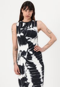 Rochie ajustată fără mâneci, cu un model tie-dye în culori alb și negru, având un design drapat și țesătură texturată, cu detalii ale cusăturilor vizibile.
