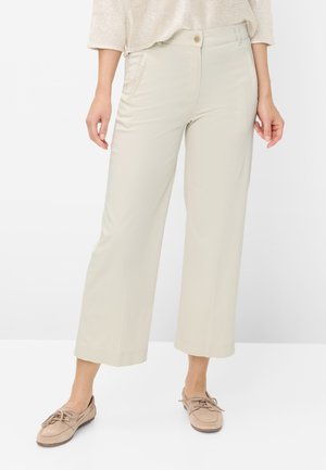 Vrouw draagt beige wijde cropped broek met voorzakken en knoopsluiting, gecombineerd met beige loafers met franjes.