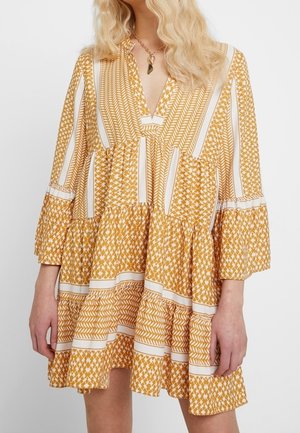 Geel patroon jurk met een v-hals, wijde mouwen en een gelaagde rok met witte accenten en geometrische ontwerpen.