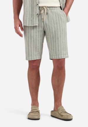 Man draagt lichtgrijze shorts met koord en verticale witte strepen, beige instapschoenen en een bijpassend kort mouw overhemd.