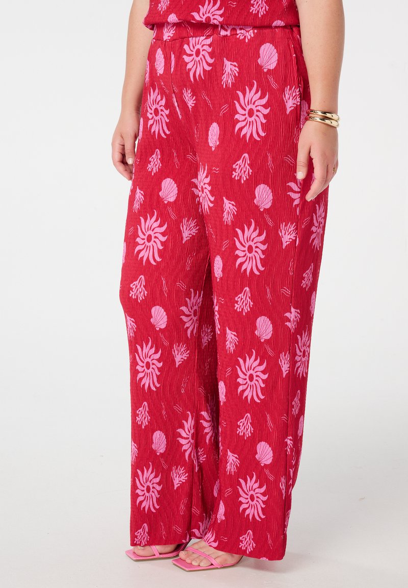 Pantalon large rouge avec un motif floral rose, comprenant des motifs de soleil et de coquillage. Fabriqué en tissu texturé, la ceinture est élastique pour le confort.