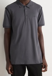 Polo shirt en charbon avec un col, trois boutons, des manches côtelées et un logo brodé. Texture lisse, coupe décontractée.