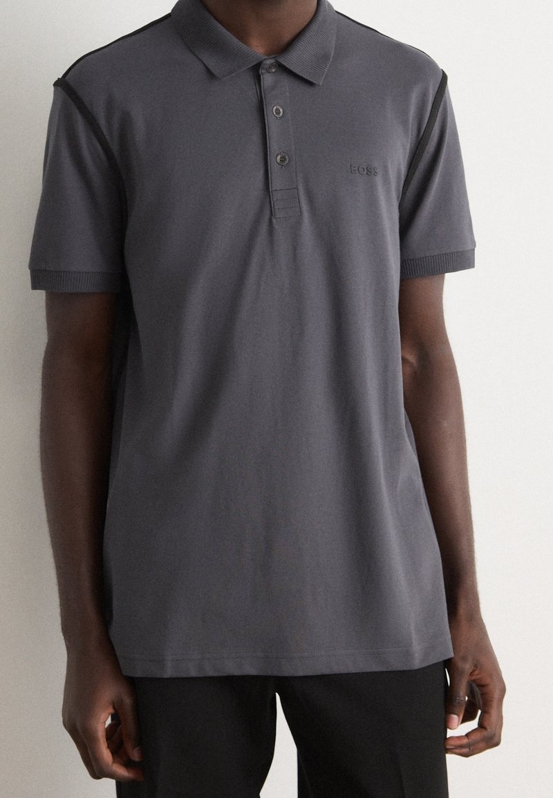 Polo shirt en charbon avec un col, trois boutons, des manches côtelées et un logo brodé. Texture lisse, coupe décontractée.