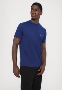 Mornarsko modra majica s kratkimi rokavi iz mehkega materiala, z okroglim izrezom in majhnim belim logotipom na levem prsnem delu. Naravna krojna oblika.