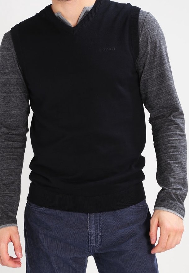 Svart v-ringad tröja med ribbad nederkant, överlagd på en grå långärmad skjorta. Tyget verkar mjukt och visar en lagerdesign med minimal varumärkesprofil.