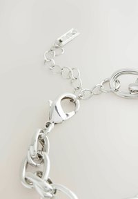 Lantă de metal argintiu cu inele ovale și rotunde, dotată cu un carabinier și un segment cu lănțișor plat. Finisaj lucios, textură netedă.