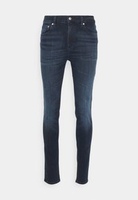 Jeans ajustados de color azul oscuro con bolsillos frontales, trabillas para cinturón y cierre de botón sobre un fondo blanco.