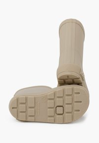 Bottes de pluie en caoutchouc beiges, montantes jusqu'au genou, avec des semelles texturées, des rainures verticales et un accent de prise douce en haut. Fabriquées en Espagne.