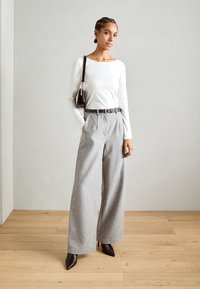 White long-sleeve top paired with high-waisted, wide-leg gray trousers. Accessorized with a dark handbag and pointed-toe high heels.