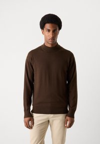 Bruine, gebreide coltrui met lange mouwen en geribbelde manchetten, gecombineerd met lichtbeige broek; gladde textuur en slim-fit vorm.