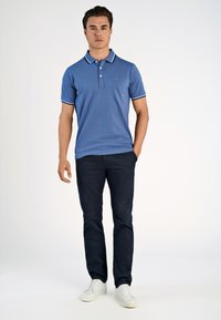 Niebieska koszulka polo z kontrastującym białym kołnierzykiem i lamówką na rękawach, zestawiona z granatowymi spodniami i białymi trampkami. Prosty, dopasowany krój.