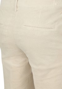 Lichtbeige corduroybroek met verticale ribbels, voorzien van twee achterzakken en een gladde textuur.