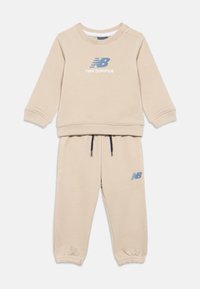 Tuta beige per bambini con felpa a maniche lunghe e polsini elasticizzati, con loghi blu di New Balance sul petto e sui pantaloni.