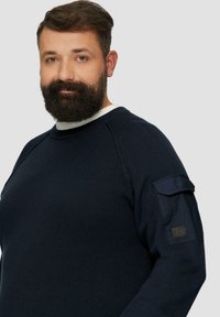 Marineblauer Strickpullover mit gerippter Textur, rundem Kragen und Schulterpatch-Details. Verfügt über einen kontrastierenden, hellen Innenkragen.