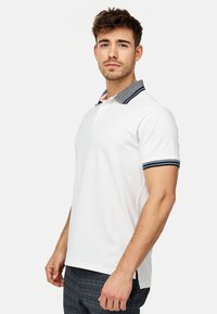 Hvid polo-shirt med korte ærmer, grå stribet krave og marineblå detaljer, med lige bund og tre-knaps lukning.