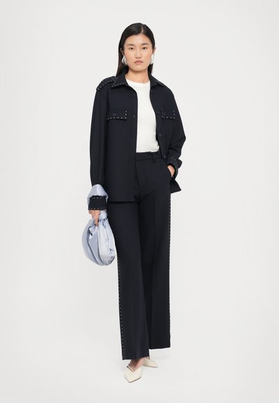 Black jacket with studded shoulders paired with a white top and black wide-leg pants. Light blue bag and cream pointed-toe shoes complete the look.