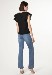 Top nero con maniche in pizzo a balze e dettaglio a chiave sul retro, abbinato a jeans a zampa blu e scarpe con tacco alto argentate.