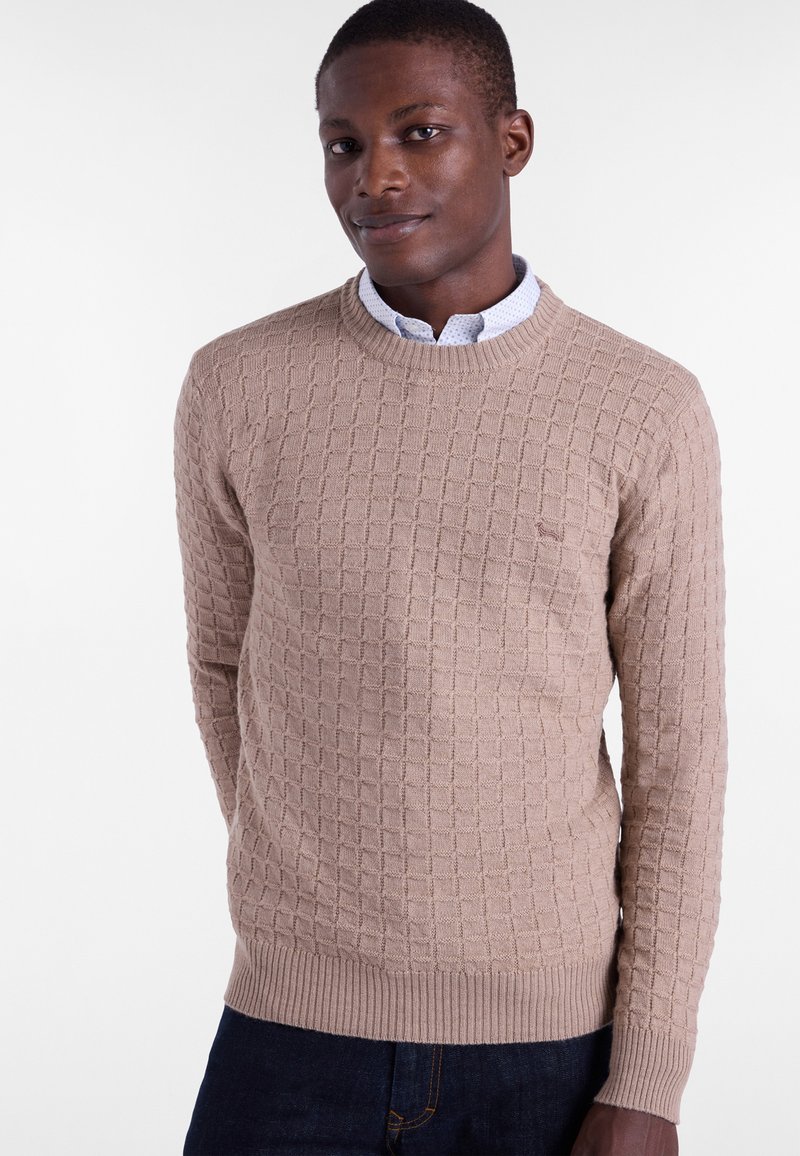 Beige knit sweater with a textured check pattern, crew neckline, ribbed cuffs, and hem, worn over a light blue collared shirt.