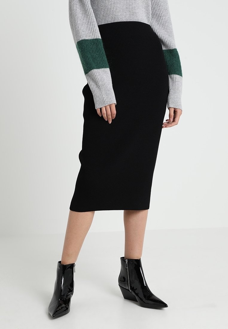 Černá žebrovaná midi sukně s přiléhavým střihem, kombinovaná se světlou šedou svetr s zelenými pruhy a lesklými černými kotníkovými botami.