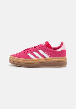Różowy but sportowy Adidas Gazelle z białymi paskami i potrójnie warstwową, grubą brązową podeszwą na białym tle.