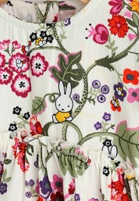 Tissu à motif floral avec un dessin animé de lapin portant une chemise jaune. Ourlet volanté, vignes vertes et diverses fleurs colorées tout au long.