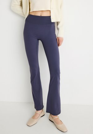 Navy flared leggings made of stretchy fabric with a high waist. Paired with light beige flats, and a cream cardigan. Smooth texture.
