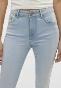 Jeans de mezclilla azul claro con una cintura alta, diseño de cinco bolsillos y un ligero desvanecimiento. Presentan un cierre de botón metálico y acentos bordados.