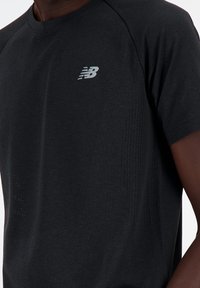 Black athletic t-shirt featuring short sleeves, a crew neck, textured fabric, and a reflective New Balance logo on the chest.