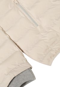 Veste matelassée beige avec une texture matelassée, dotée d'une fermeture éclair latérale et de poignets en maille grise côtelée. Fini lisse et forme structurée.