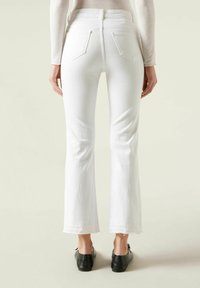 Jeans blancos acampanados de cintura alta, con bolsillos traseros y un dobladillo sin rematar. La tela parece texturizada y ligeramente elástica.