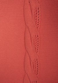 Tejido de punto en color coral con un patrón trenzado central y detalles de puntada abierta, que proporciona textura e interés visual.