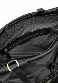 Black leather handbag interior featuring a zip pocket and a patterned nylon lining with horizontal stripes. Gold-tone hardware accents.