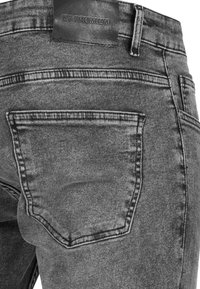 Jeans de mezclilla gris con una textura suave, que cuentan con un bolsillo trasero y una etiqueta de cuero negro cosida en la cinturilla.