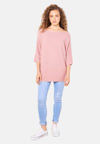 Übergroßer rosa Strickpullover mit weitem Ausschnitt und Dreiviertelärmeln, kombiniert mit hellblauen Skinny-Jeans und weißen Sneakers.