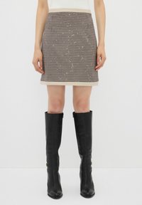 Jupe à motif pied-de-poule avec une taille beige, longueur genoux, complétée par des bottes noires à hauteur de genou avec une finition lisse et une fermeture éclair.