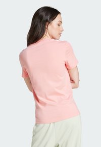 T-shirt de algodão rosa claro com gola redonda e mangas curtas, apresentando uma textura suave e uma forma ajustada típica.