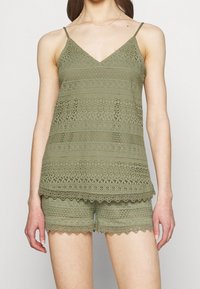 Svetle olivový top s krajkovým vzorem a nastavitelními ramínky, doplněný šortkami s krajkovými detaily, oboje s jemnou texturou a zvlněnými okraji.