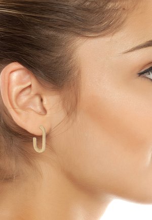 Orecchini a forma di U in tonalità oro esposti sull'orecchio di un modello, caratterizzati da una finitura liscia e un design minimalista che evidenzia la forma.